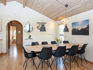 Un espace repas avec une table en bois et des chaises noires, un grand miroir et des luminaires suspendus.