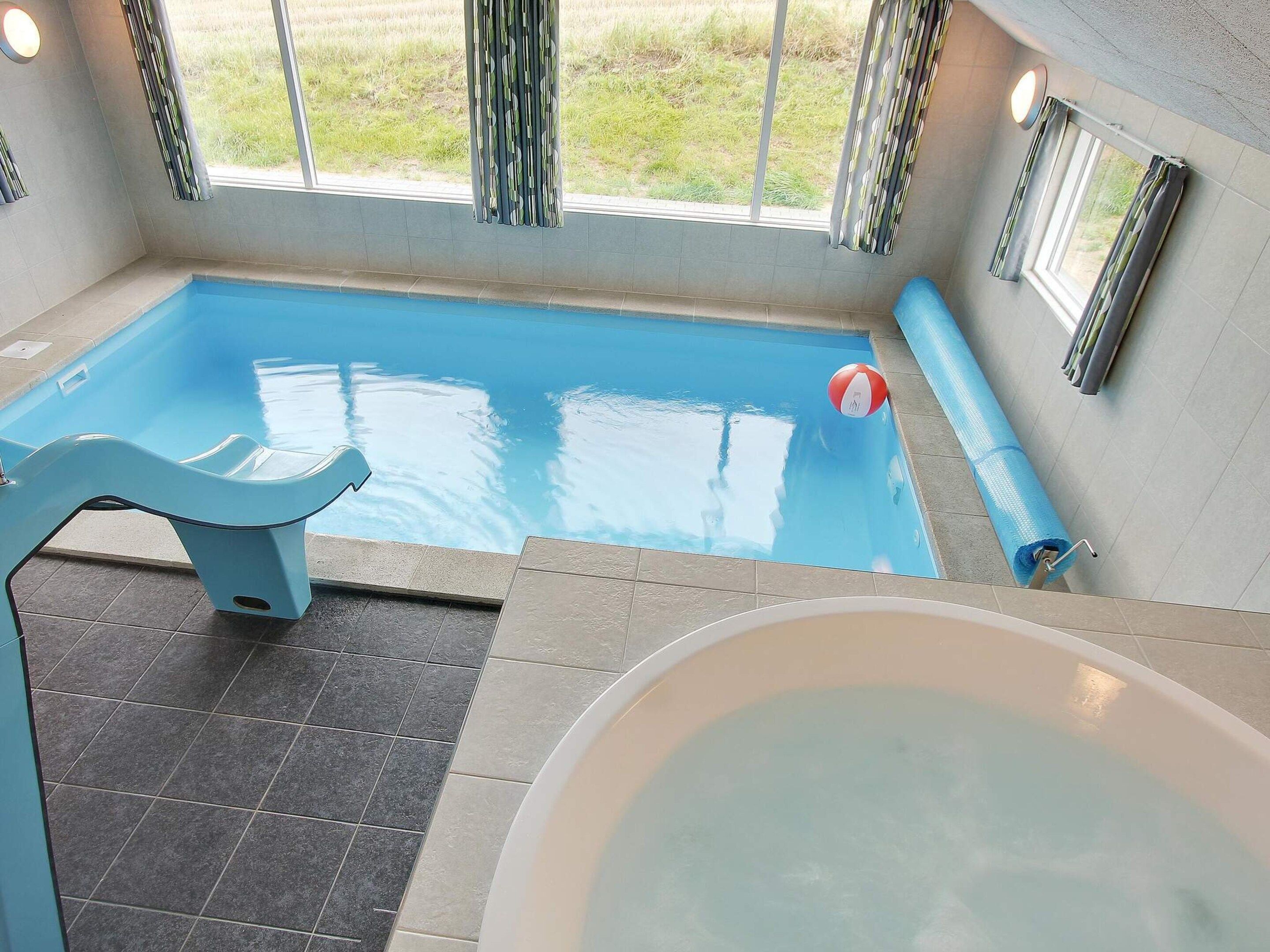 A swimming pool with a blue chair, a white tub, and a view of the outdoors.