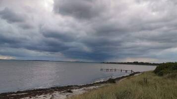 A beach with a wooden pier extending into calm waters, surrounded by grassy dunes.