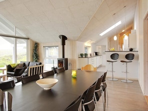A modern kitchen with a central island, a dining area with a long table, and a cozy seating area with a fireplace. - 5 Star Holiday Home in Sydals (Sydals)