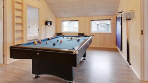 Une table de billard dans une pièce aux murs en bois et au plafond en pente.