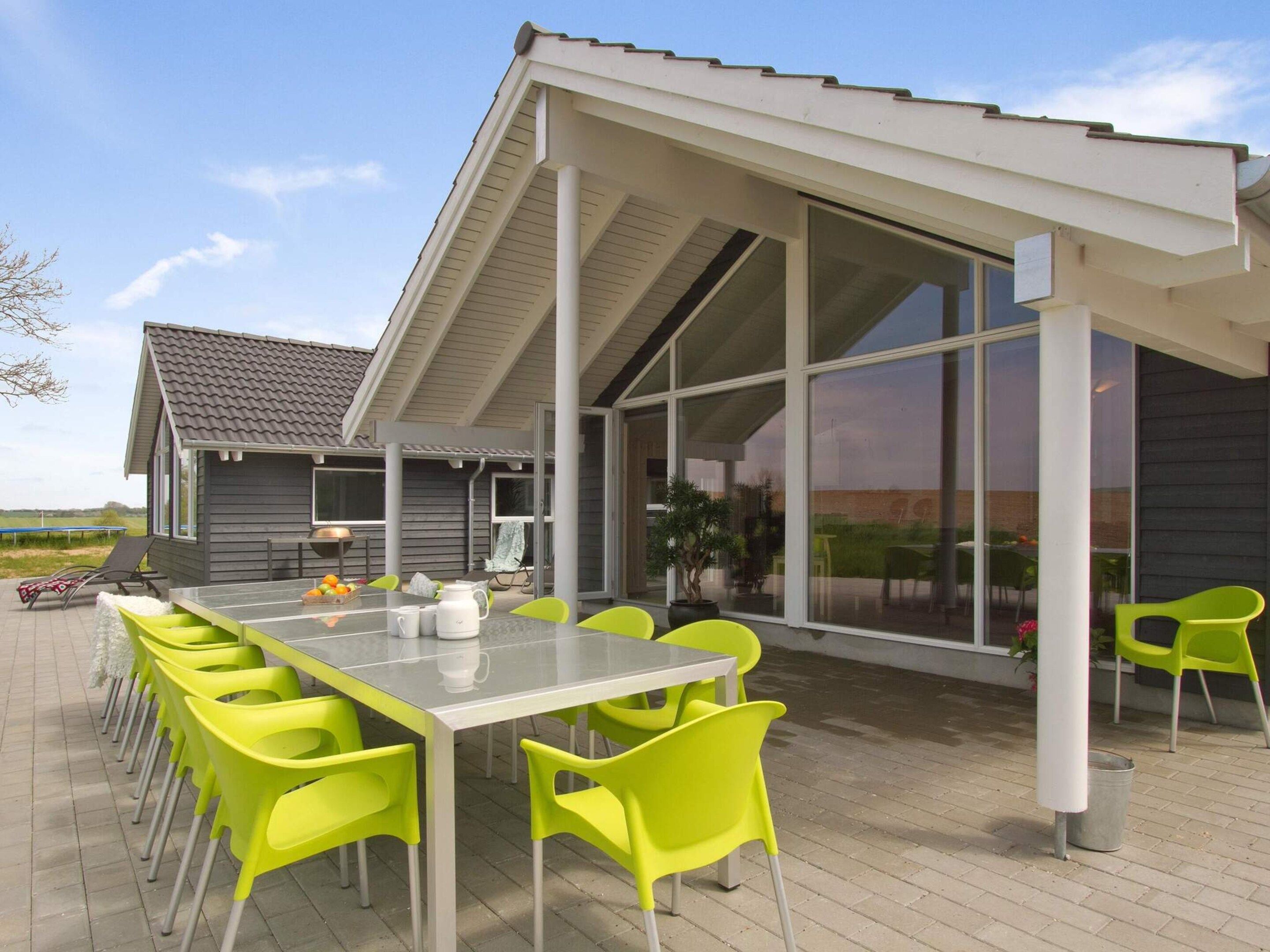 Ein moderner Essbereich im Freien mit einem langen Tisch und leuchtenden Stühlen, einer überdachten Terrasse und Blick auf die Landschaft.