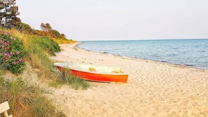 Ein sandiger Strand mit einem roten Boot und einer Holzbank.