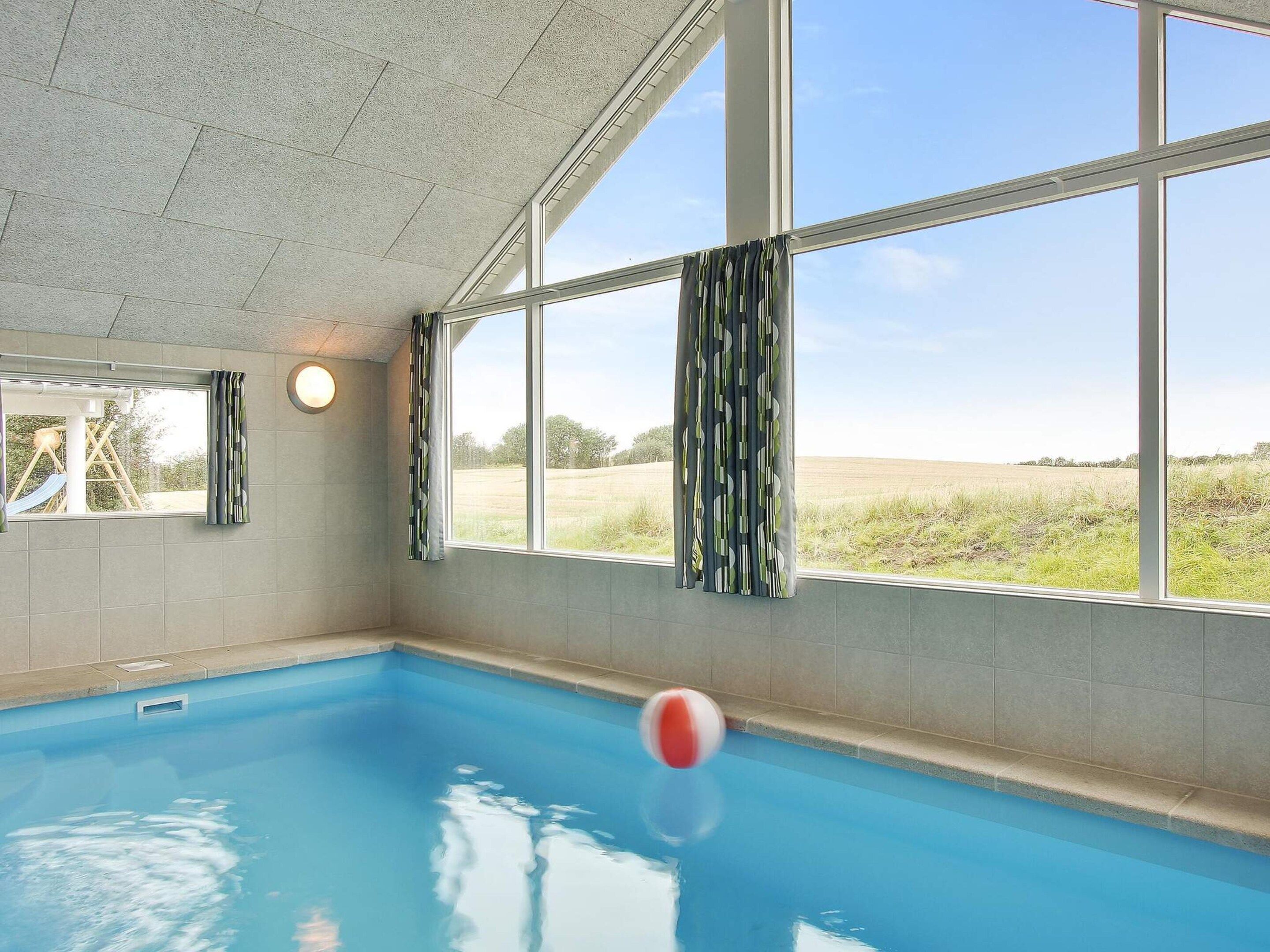 Ein Hallenbad mit Blick auf ein grünes Feld durch große Fenster.