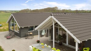 Une maison moderne dotée d’un patio couvert, d’un coin repas avec des chaises jaune vif et d’une petite cuisine extérieure.