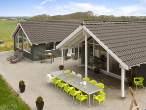 A modern house with a covered patio, a dining area with bright yellow chairs, and a small outdoor kitchen.