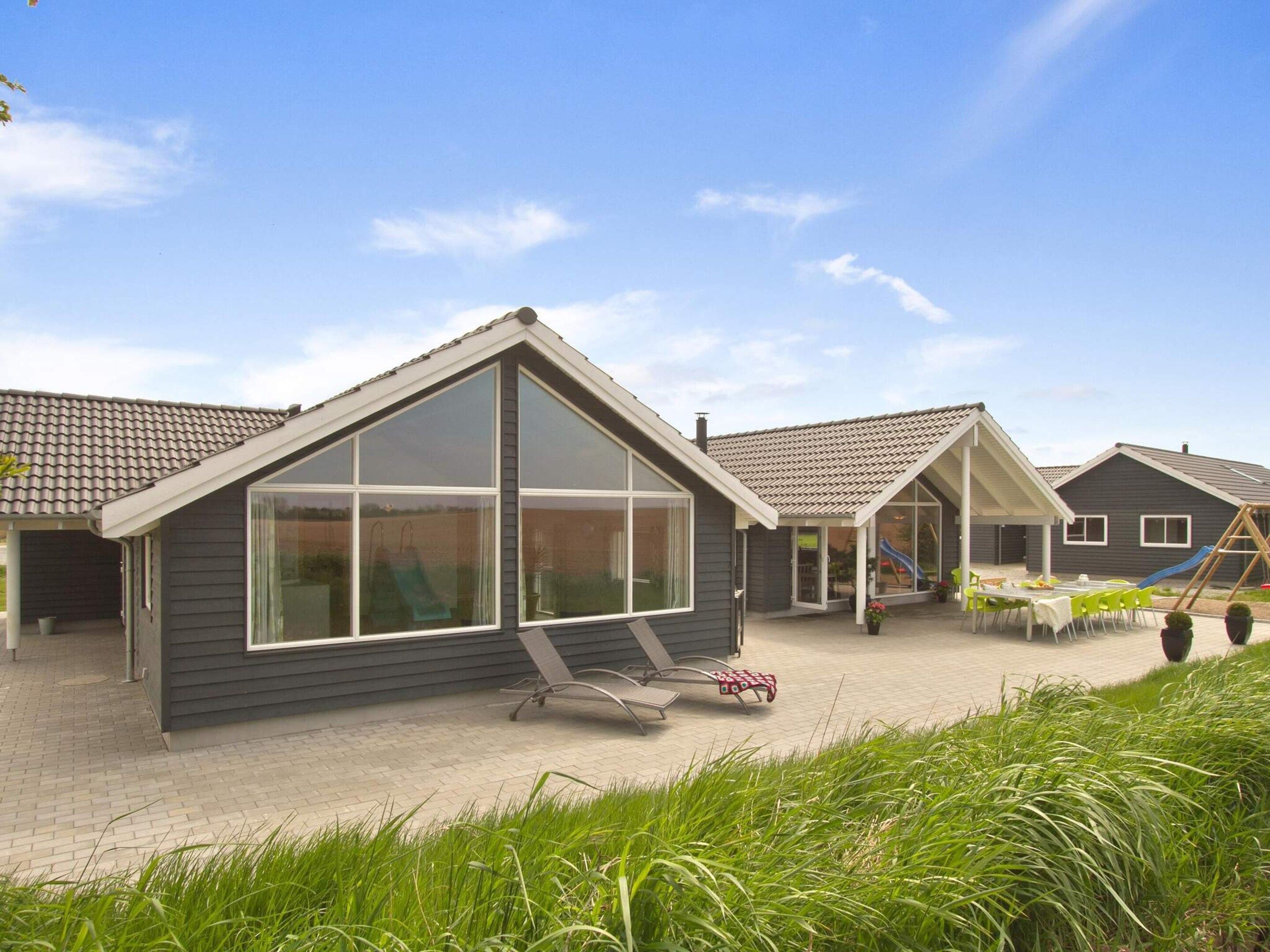 Une maison moderne dotée d’une grande baie vitrée, d’un patio couvert et d’un espace de jeux avec un toboggan.