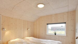 Ein Schlafzimmer mit zwei Betten, Holzwandverkleidung, einem Fenster mit Blick und einer Deckenleuchte.