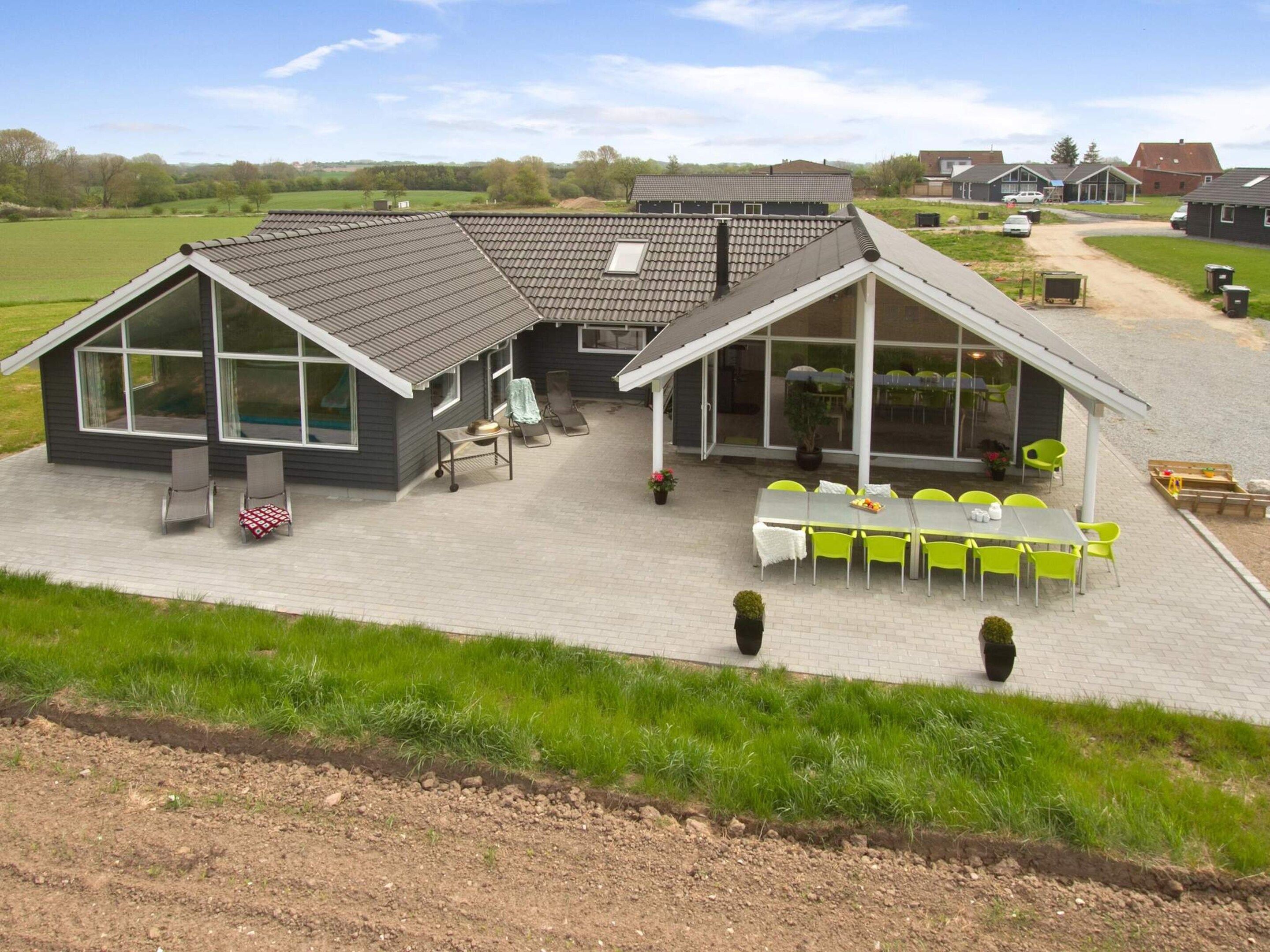 Ein modernes Haus mit einer Terrassenfläche, Sitzgelegenheiten im Freien und Blick auf die umliegende Landschaft.