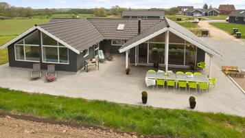 Ein modernes Haus mit einer Terrassenfläche, Sitzgelegenheiten im Freien und Blick auf die umliegende Landschaft.