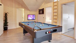 Une table de billard avec des billes, un téléviseur et un jeu de fléchettes dans une pièce aux murs en bois et au plafond en pente.
