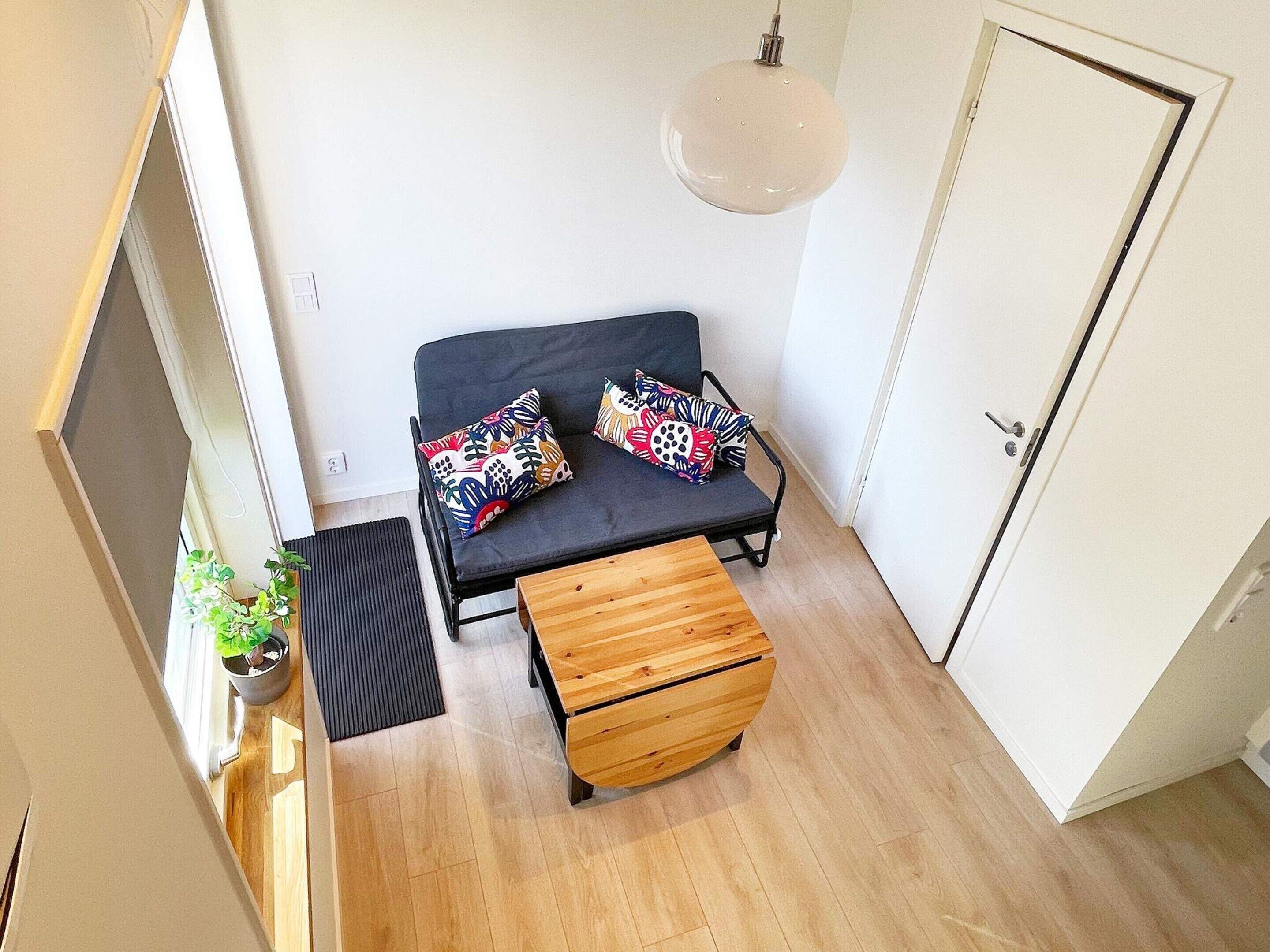 A compact room with a bed, a bench, a hanging light fixture, and a door.