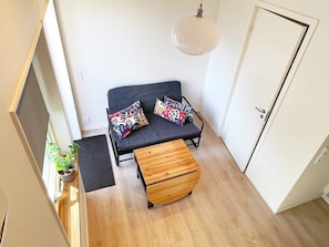 Habitación pequeña con cama, banco, lámpara colgante y una puerta.