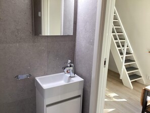A bathroom with a white sink, a mirror, and a staircase leading to another level.