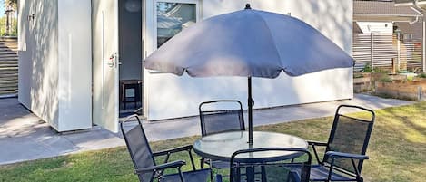 A patio with a round table and four chairs, an umbrella, and a white building with a sliding door.