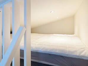 Una habitación pequeña con cama individual, techo inclinado e iluminación empotrada.
