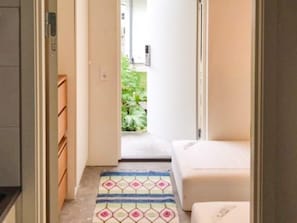 A narrow hallway with a patterned rug leading to a room with a bed.
