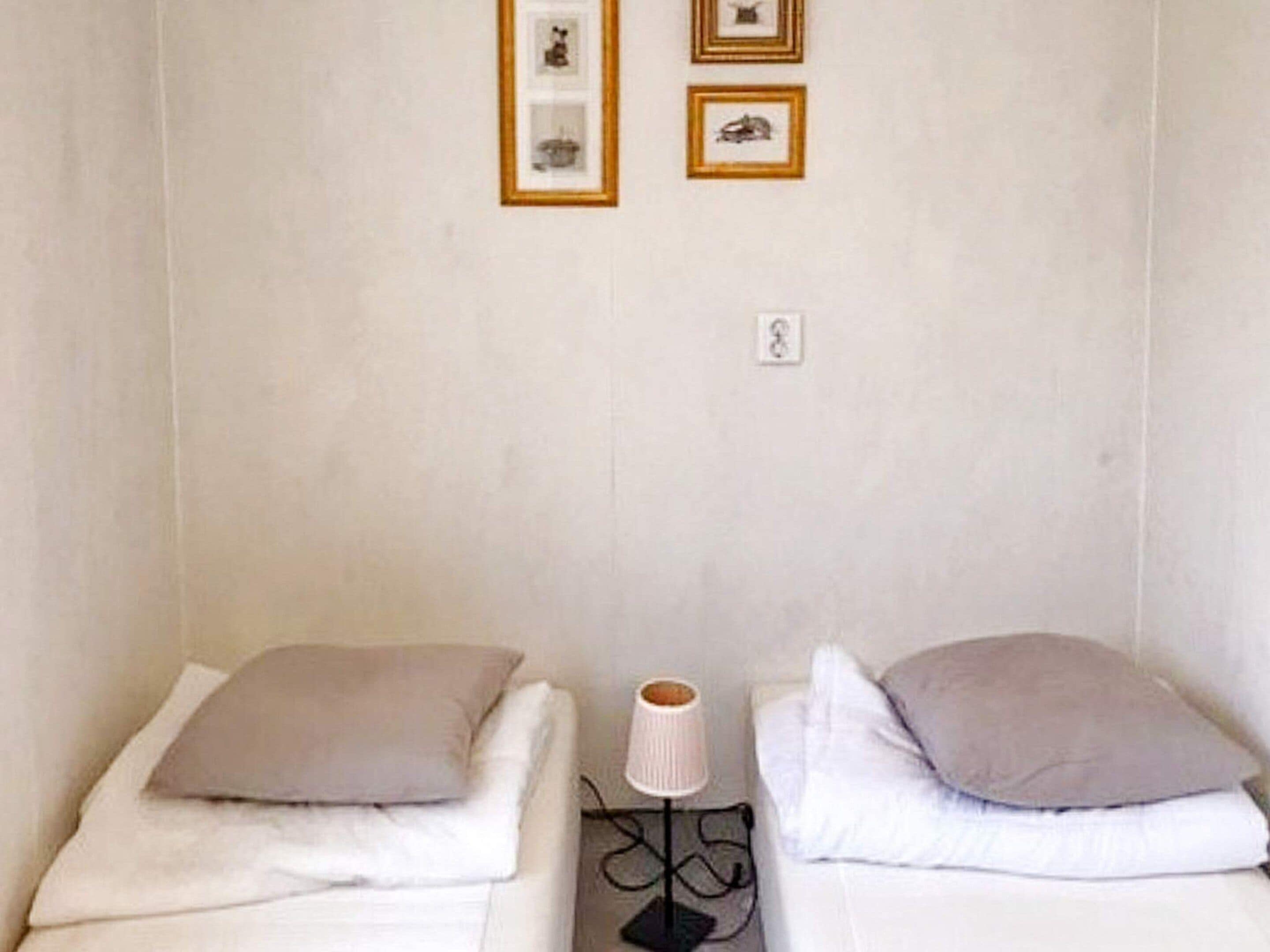 Quarto de hotel com duas camas, cada uma com travesseiro e luminária.