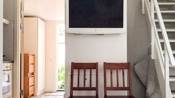 A room with a television mounted on the wall, a wooden table, two chairs, and a staircase.
