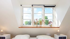 A bedroom with a skylight, two bedside tables, a bed with white bedding, and a window with a view of trees.