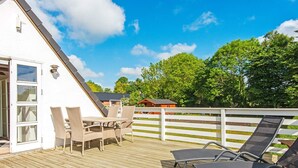 A wooden deck with outdoor furniture, a white building with a sloped roof, and a white fence.