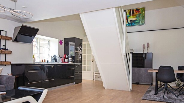 A modern kitchen with black cabinets, a dining area with a table and chairs, and a large window providing natural light.