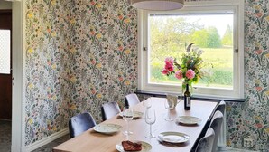 A dining room with a floral wallpaper, a wooden table set for four, and a window with a view of a garden. - 8 Person Holiday Home in Moheda (Moheda)