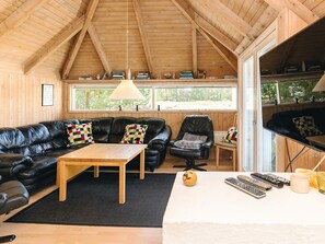Una habitación acogedora con techo de madera, un sofá de cuero negro, una mesa de centro de madera y una ventana con vistas a la vegetación.