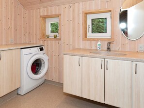 A compact kitchen with wooden cabinets, a washing machine, a sink, and a window with a view of greenery. - 8 Person Holiday Home in Fjerritslev (Fjerritslev)
