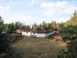 A white cabin with a thatched roof surrounded by coniferous trees. - 8 Person Holiday Home in Fjerritslev (Fjerritslev)