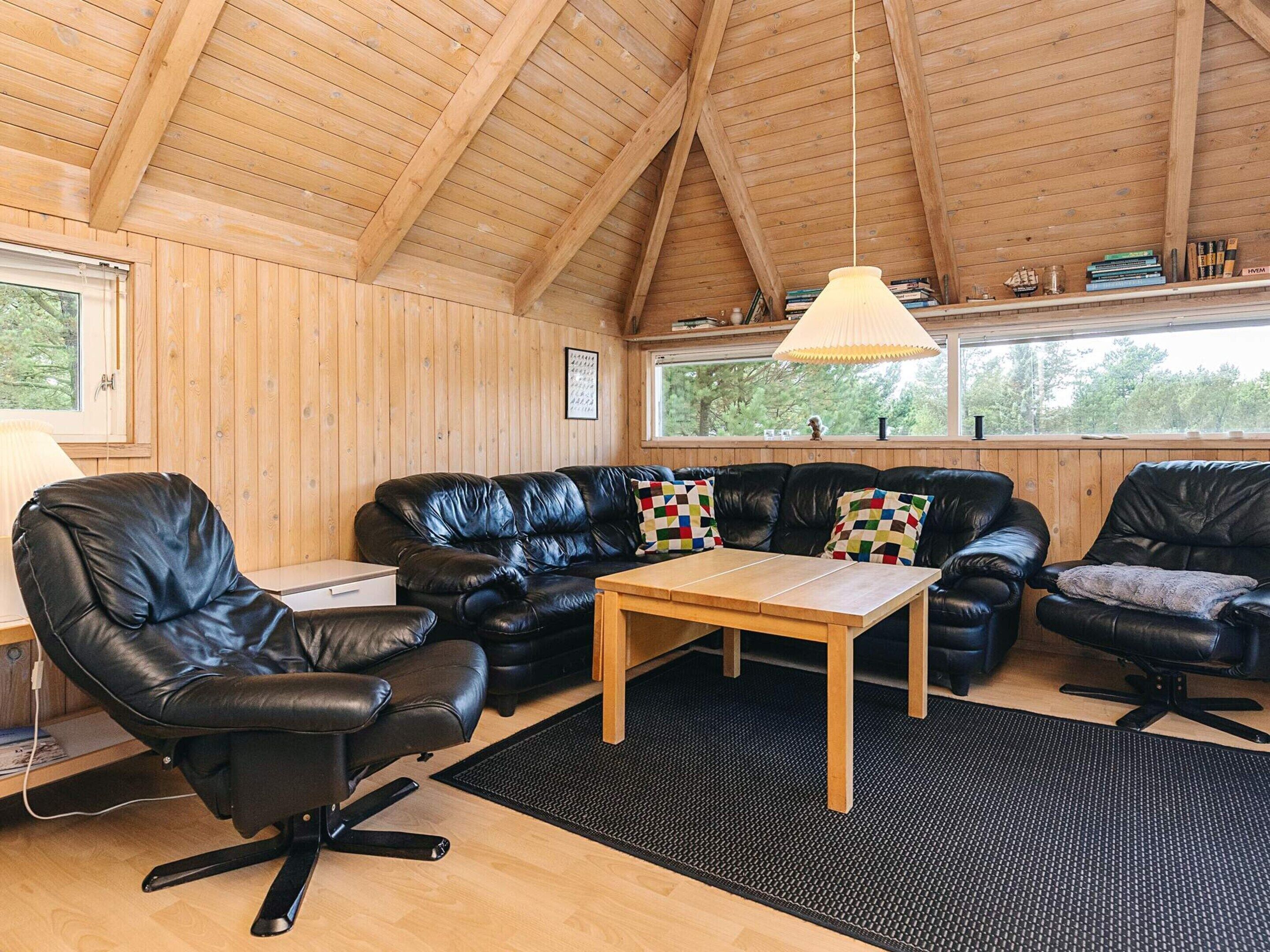 A cozy room with a wooden ceiling, a black leather sofa, a wooden coffee table, and a black office chair.