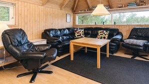 A cozy room with a wooden ceiling, a black leather sofa, a wooden coffee table, and a black office chair.