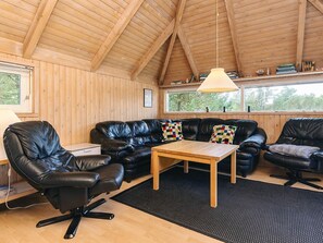 Una habitación acogedora con techo de madera, un sofá de cuero negro, una mesa de centro de madera y una silla de oficina negra.