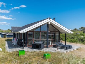 A modern house with a large glass window, a deck, and outdoor furniture. - 6 Person Holiday Home in Fano (Fano)