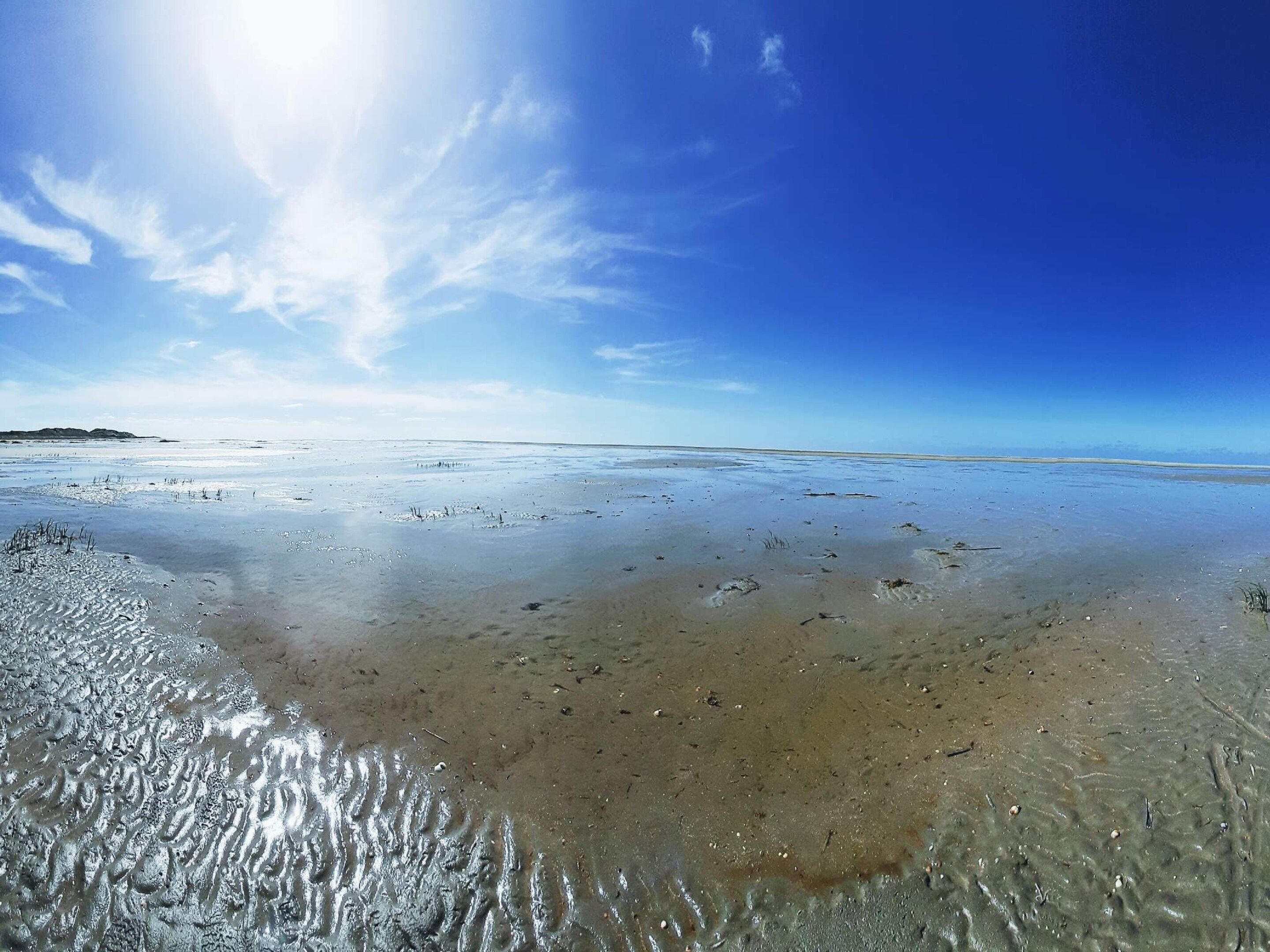 A beach with clear water, a distant landmass, and a bright sky.