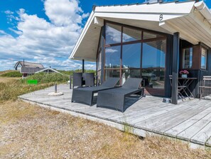 A modern beach house with a large glass window, a wooden deck, and outdoor seating. - 6 Person Holiday Home in Fano (Fano)