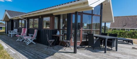 A covered outdoor area with a wooden deck, seating, and a glass enclosure.