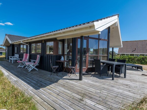 A covered outdoor area with a wooden deck, seating, and a glass enclosure.