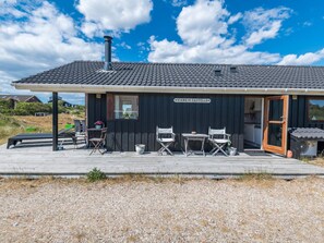 A black building with a tiled roof, a sign reading 'VIANA DE CASTELLO', outdoor seating with chairs and a table, and a gravel ground. - 6 Person Holiday Home in Fano (Fano)