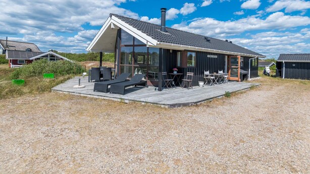 Et moderne hus med en overdækket terrasse, udendørs møbler og et stort vindue med udsigt over landskabet.