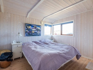 A bedroom with a single bed, a nightstand, a lamp, a painting, and a window.