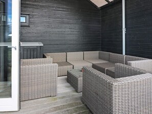 A covered outdoor seating area with wicker furniture and a dark wooden wall. - 6 Person Holiday Home in Hadsund (Hadsund)