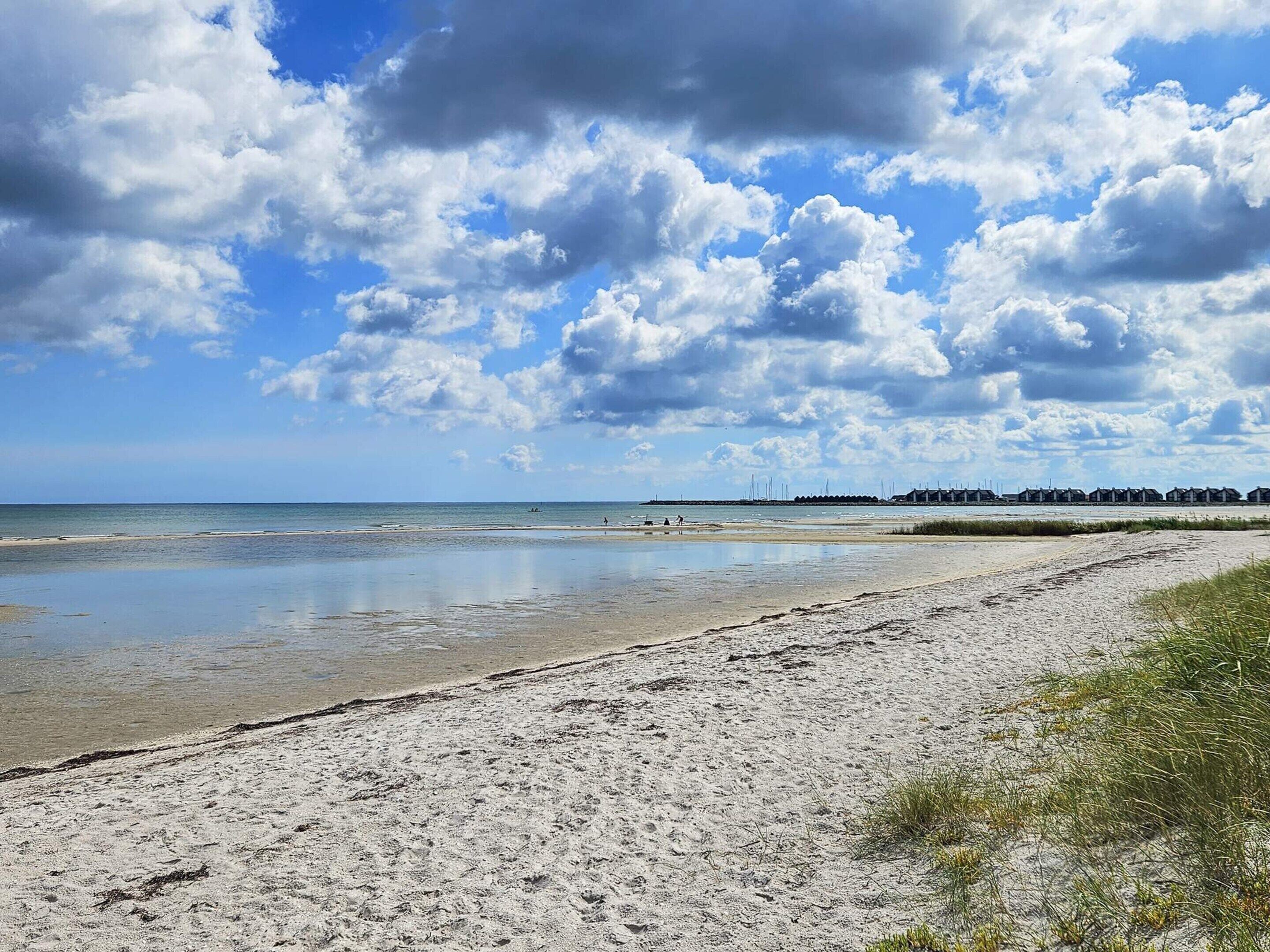 A beach with a sandy shore, a calm sea, and a partly cloudy sky.