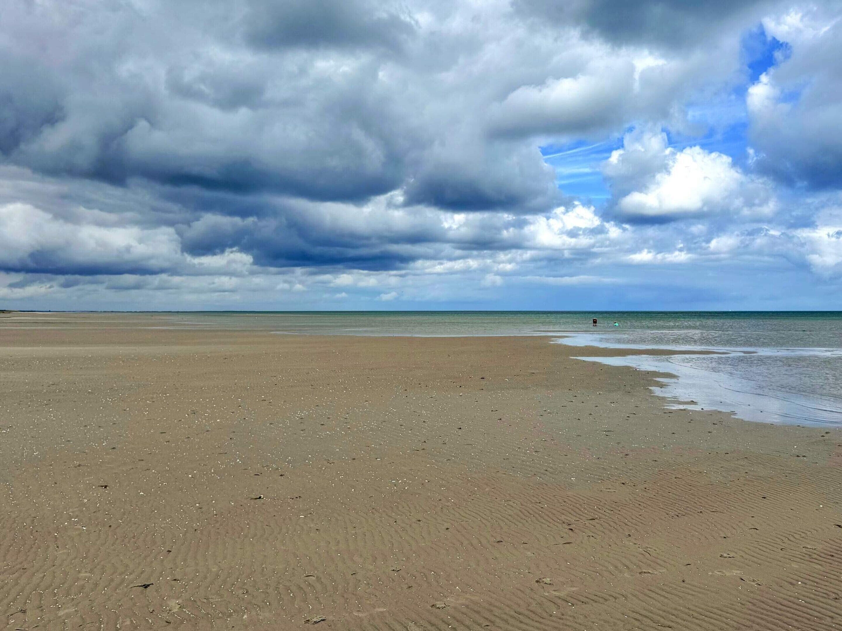 Una extensa playa de arena fina con un cielo amplio y el océano.