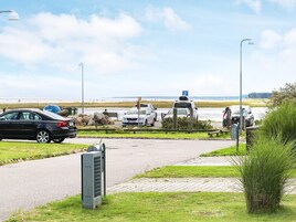 Un estacionamiento con coches, un sendero peatonal y un campo de césped al fondo.