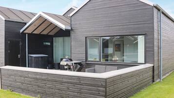 A modern house with a sloped roof, a large window, and a patio area with outdoor furniture.