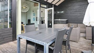 An outdoor dining area with a table and chairs, a wicker sofa, and a ceiling with wooden beams.