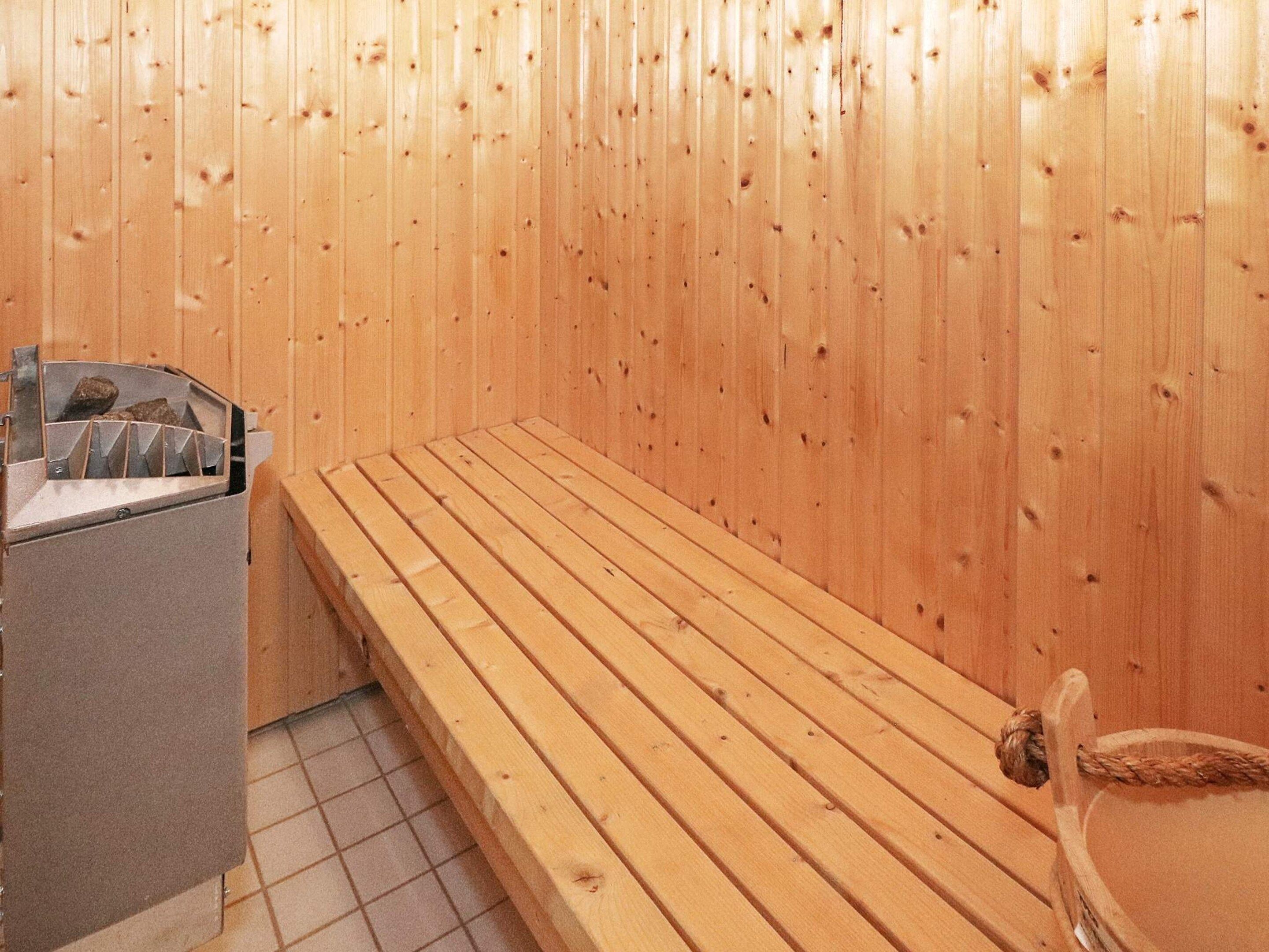 A sauna room with a wooden bench and a stone basin.
