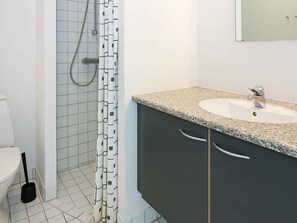 Un baño con lavamanos blanco, muebles oscuros y ducha con cortina estampada.
