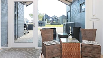 Un espacio de estar al aire libre techado, con mobiliario de mimbre y una mesa de vidrio, con vista a un barrio residencial.